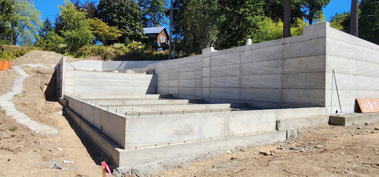 Freshly poured concrete foundation and retaining walls stepping up a wooded hillside